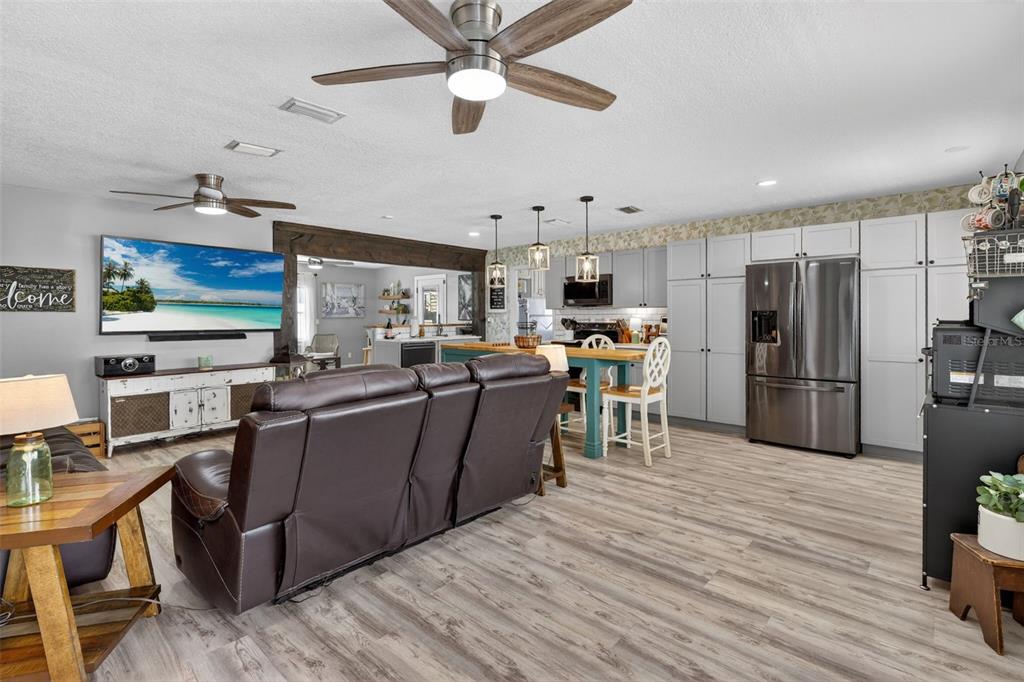 An open-concept living room and kitchen featuring light wood flooring and a brown leather sofa — 2026 7TH COURT SW, VERO BEACH, FL