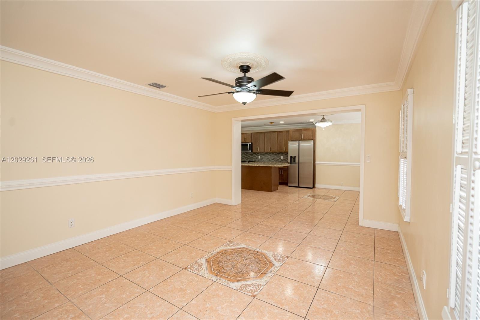 An empty room with tan tile floors and a ceiling fan leads into a kitchen — 5613 Pierce St # 1, Hollywood FL 33021, HOLLYWOOD, FL