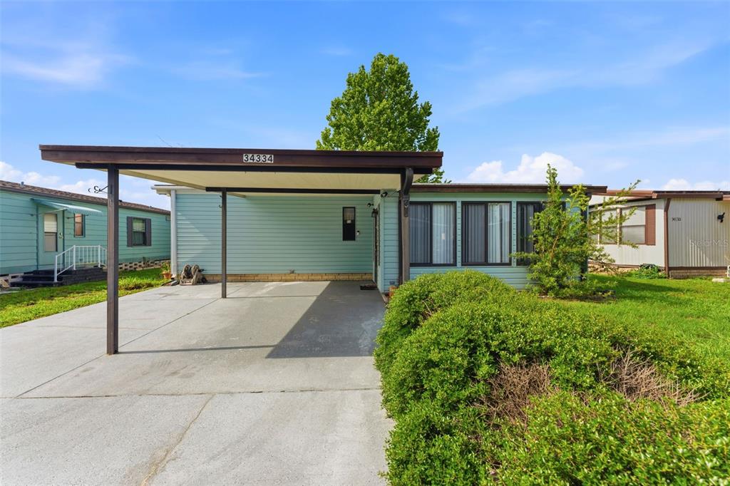 A light blue manufactured home features a concrete driveway and a covered carport — 34334 COUNTRYSIDE DRIVE, WESLEY CHAPEL, FL