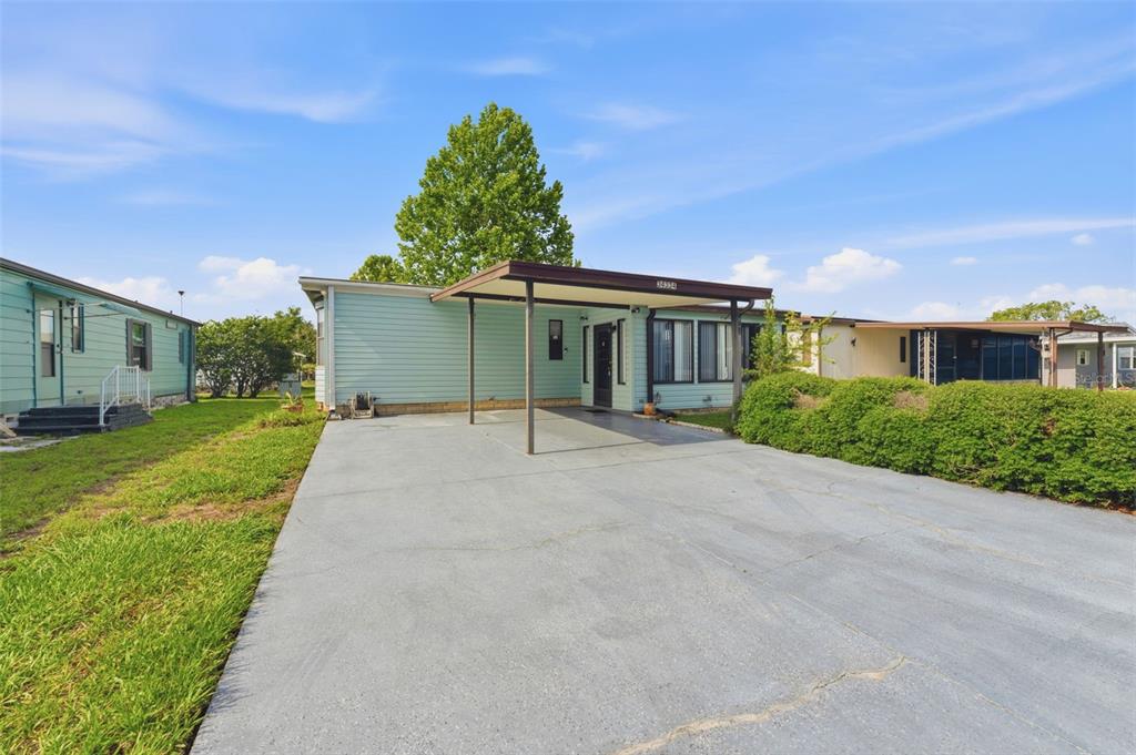 A light blue mobile home features a concrete driveway and a covered carport entrance — 34334 COUNTRYSIDE DRIVE, WESLEY CHAPEL, FL