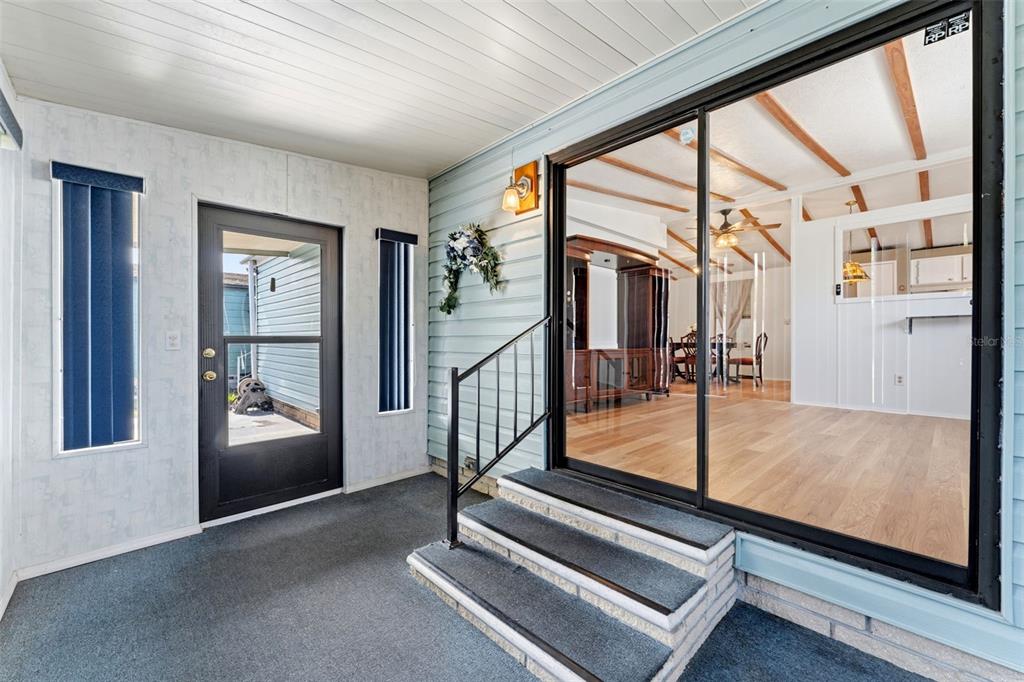 A covered porch with gray carpeting, a black storm door, and steps leading to sliding doors — 34334 COUNTRYSIDE DRIVE, WESLEY CHAPEL, FL