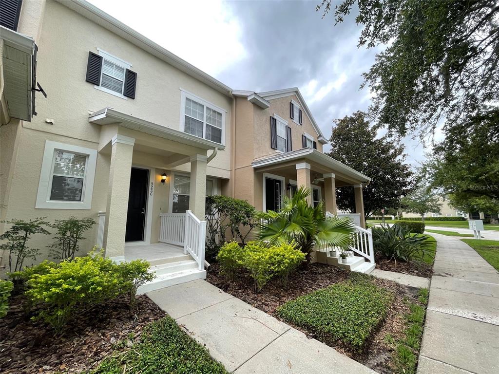 A two-story townhouse exterior with beige stucco, black shutters, and a covered front porch — 9236 CARDINAL MEADOW TRAIL, ORLANDO, FL