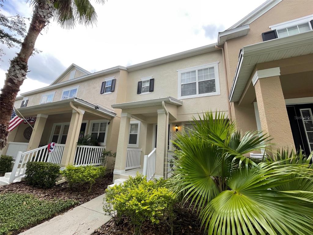A low-angle exterior view of a multi-story townhouse with beige stucco siding and palm trees — 9236 CARDINAL MEADOW TRAIL, ORLANDO, FL