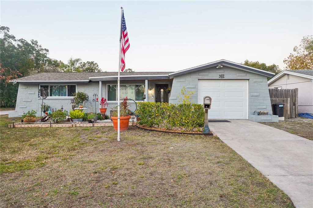 A single-story gray house with a front-facing garage, a flag pole, and a landscaped yard — 7615 CUMBER DRIVE, NEW PORT RICHEY, FL
