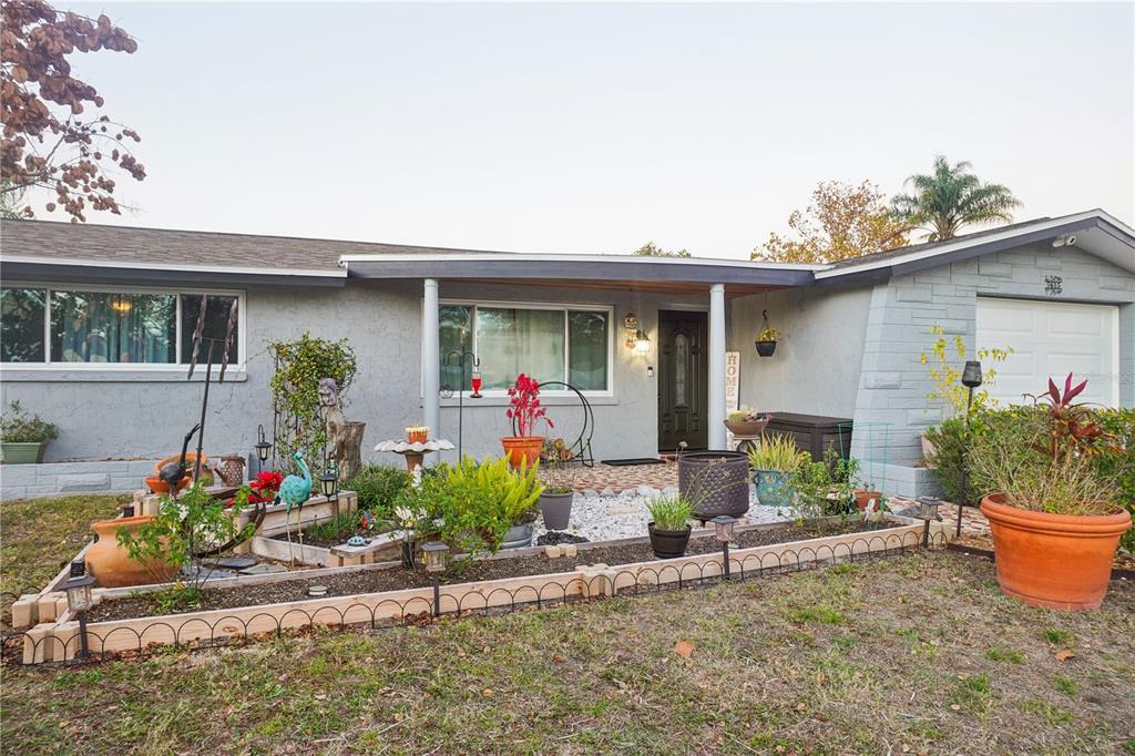 A single-story house features a gray exterior, a front porch, and a landscaped garden bed — 7615 CUMBER DRIVE, NEW PORT RICHEY, FL