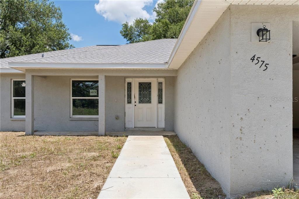 A single-story house exterior features a concrete walkway leading to a white front door — 4575 E WALKER STREET, INVERNESS, FL