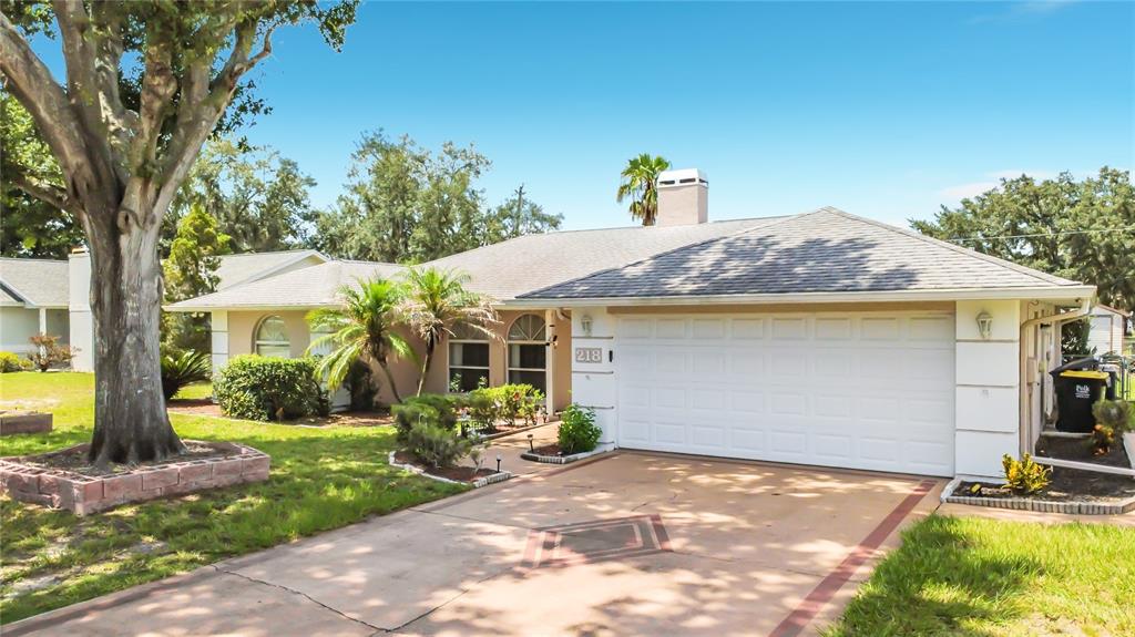 A single-story house with a white garage, beige stucco exterior, and a paved driveway — 218 GLENRIDGE LOOP N, LAKELAND, FL