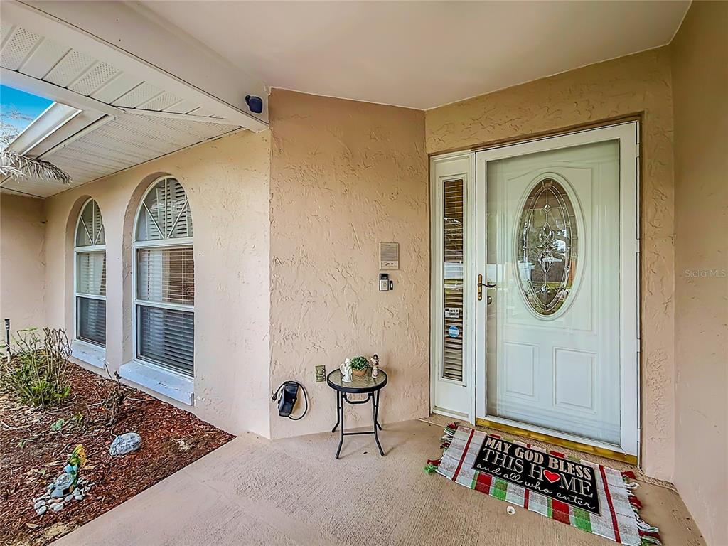 A covered entryway features a white front door with an oval glass insert and a doormat — 218 GLENRIDGE LOOP N, LAKELAND, FL