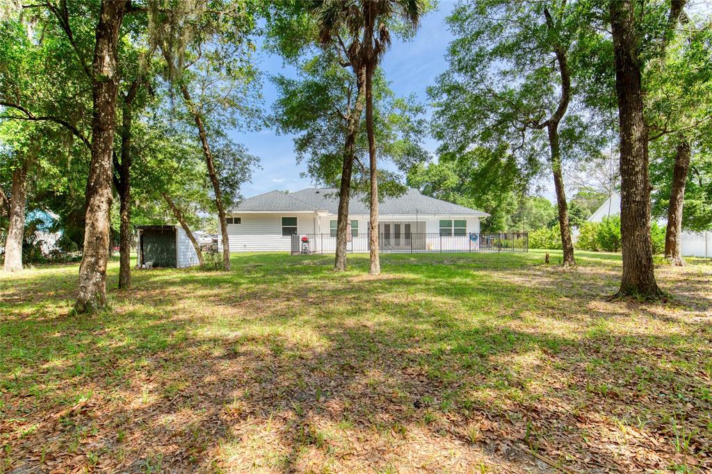 A white single-story house with a fenced backyard sits among many tall trees — 15 MAPLE STREET, FLAGLER BEACH, FL