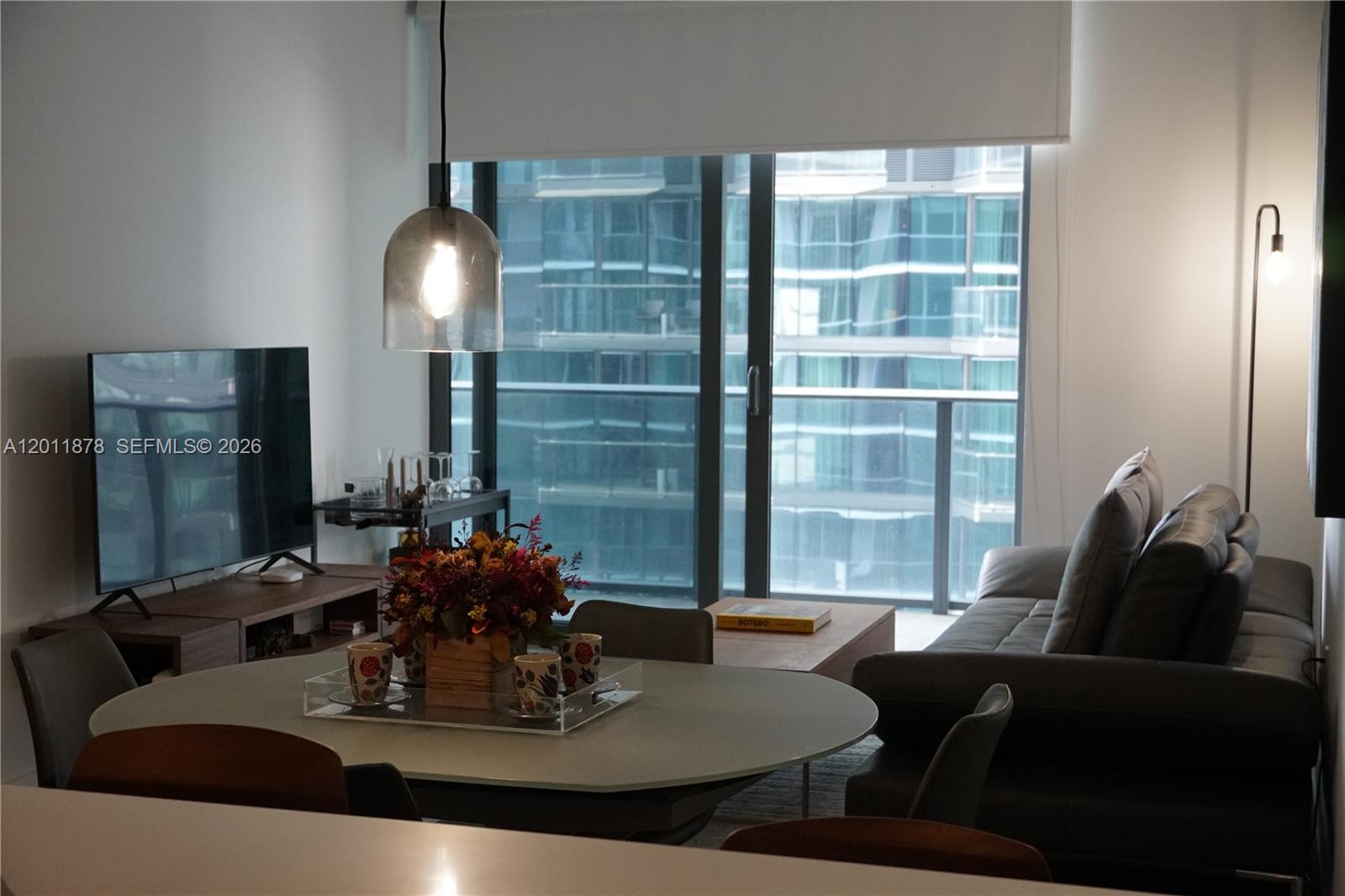 A modern living and dining area features a grey sofa, oval table, and floor-to-ceiling windows — 801 S Miami Ave # 2306, Miami FL 33130, MIAMI, FL