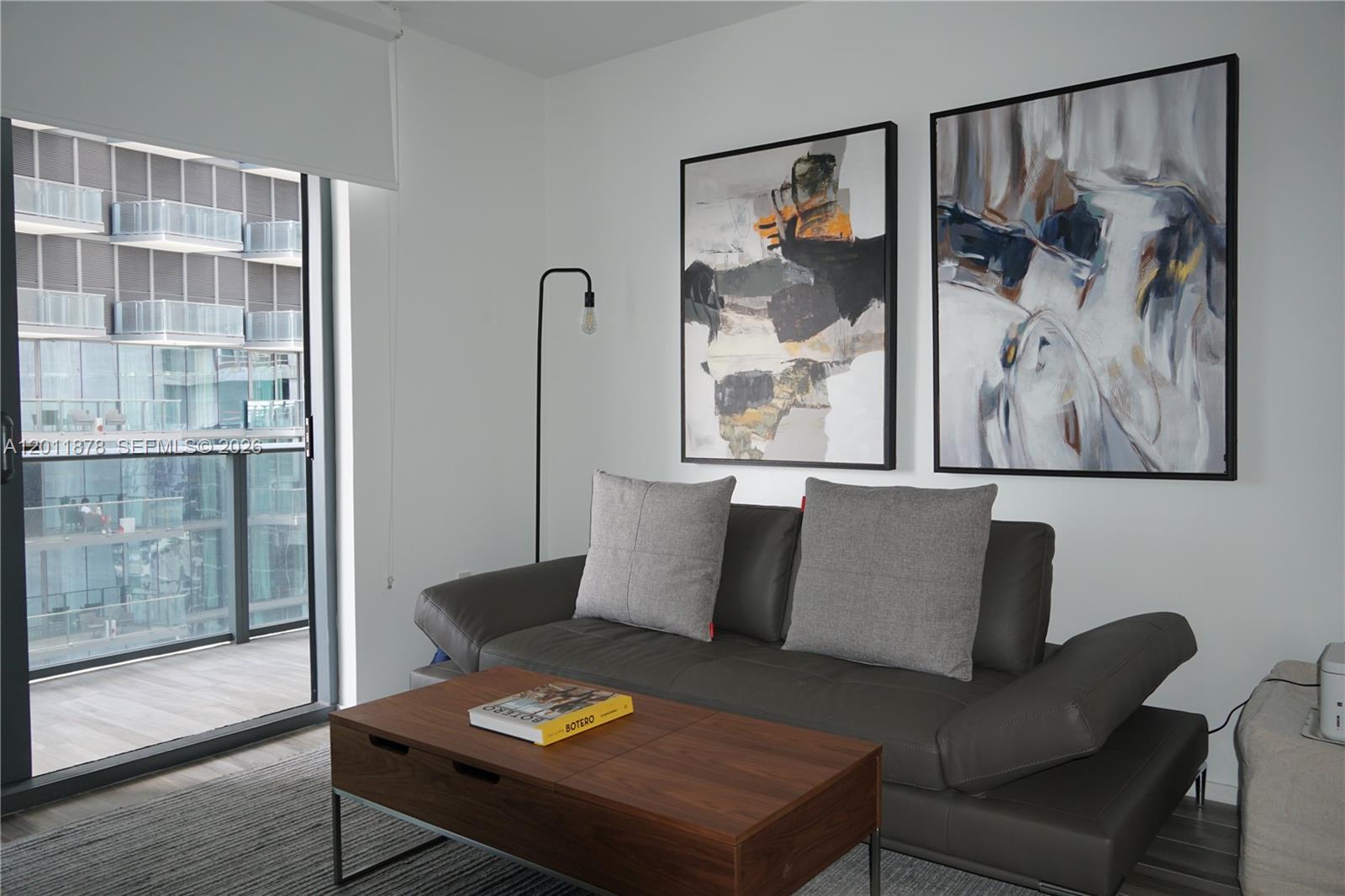 A modern living room features a grey leather sofa, wooden coffee table, and abstract wall art — 801 S Miami Ave # 2306, Miami FL 33130, MIAMI, FL
