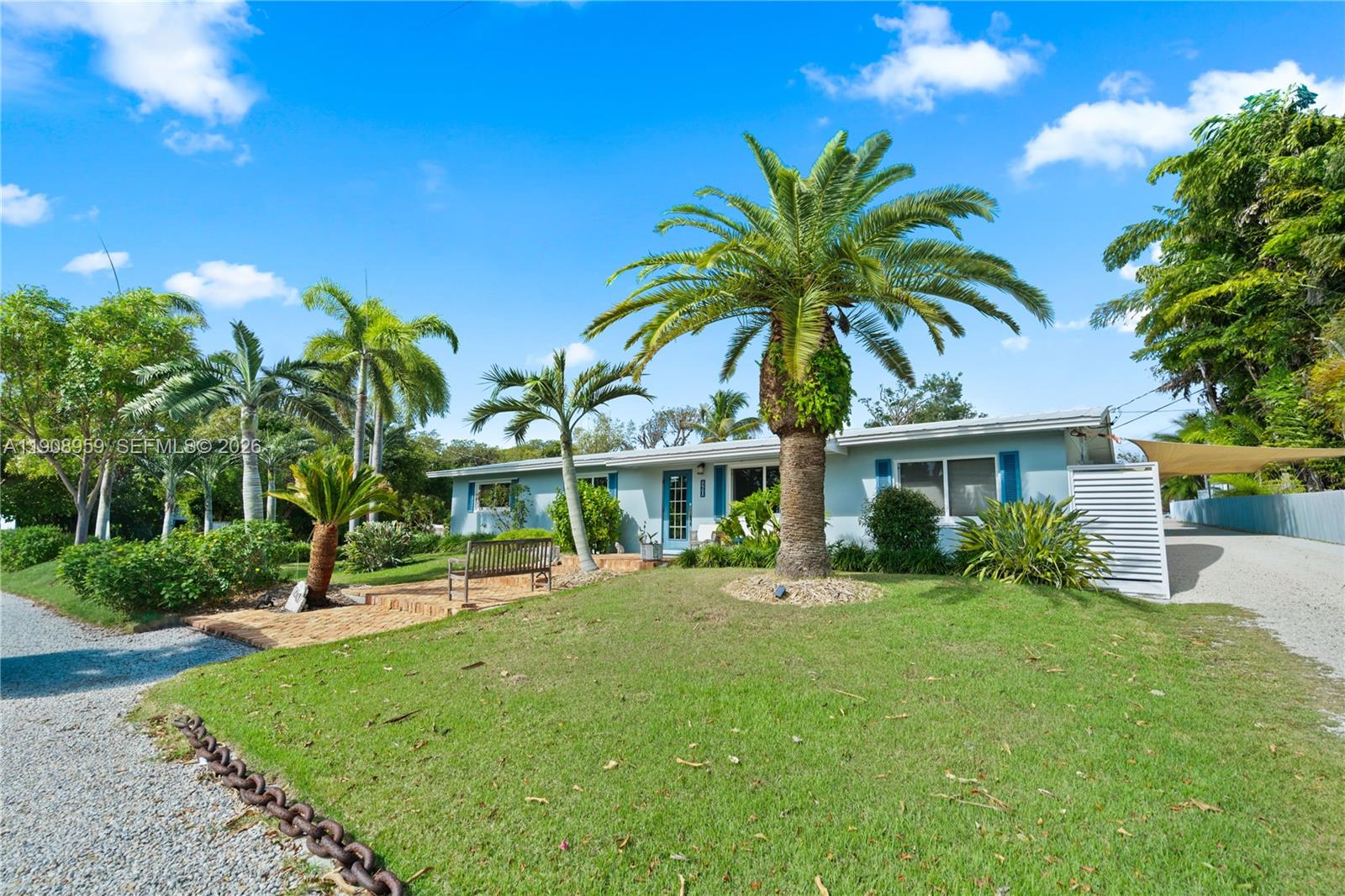 A light blue single-story house features a palm-filled front yard and a gravel driveway — 160 Ridge St, Tavernier FL 33070, TAVERNIER, FL