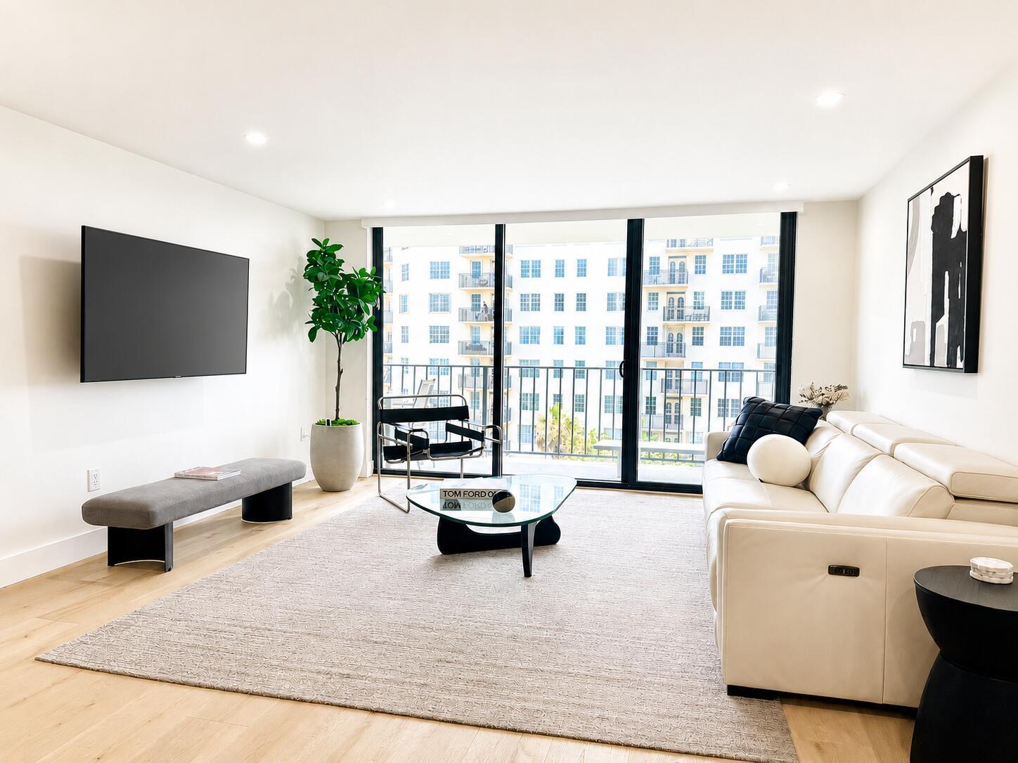 A modern living room features a white sofa, glass coffee table, television, and balcony view — 3460 S Ocean Boulevard # 4150, Palm Beach FL 33480, PALM BEACH, FL