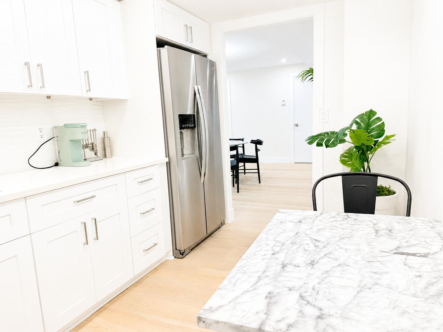 A white kitchen features a stainless steel refrigerator, marble-topped island, and light wood flooring — 3460 S Ocean Boulevard # 4150, Palm Beach FL 33480, PALM BEACH, FL