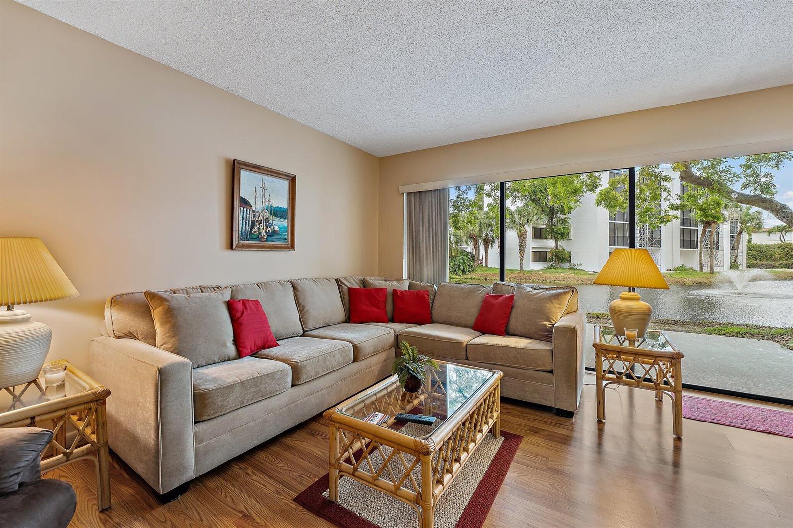 A living room with a beige sectional sofa, rattan tables, and a view of a pond — 1605 S Us Highway 1 # B104, Jupiter FL 33477, JUPITER, FL