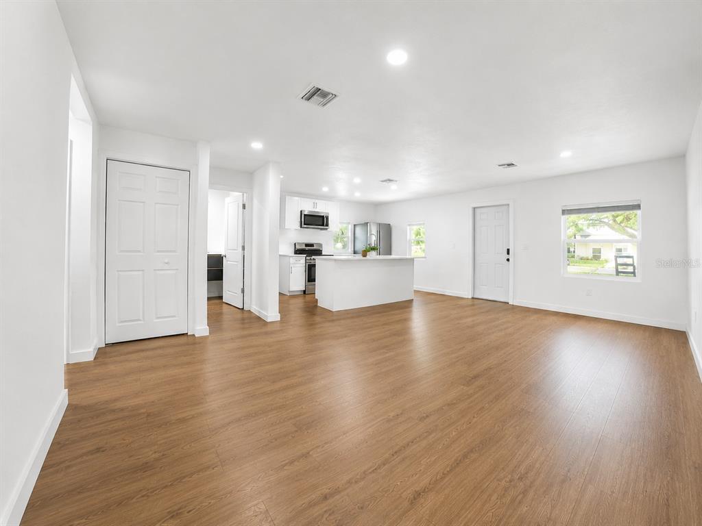 An open-concept living area features light wood flooring, white walls, and a modern kitchen island — 9212 N BROOKS STREET, TAMPA, FL
