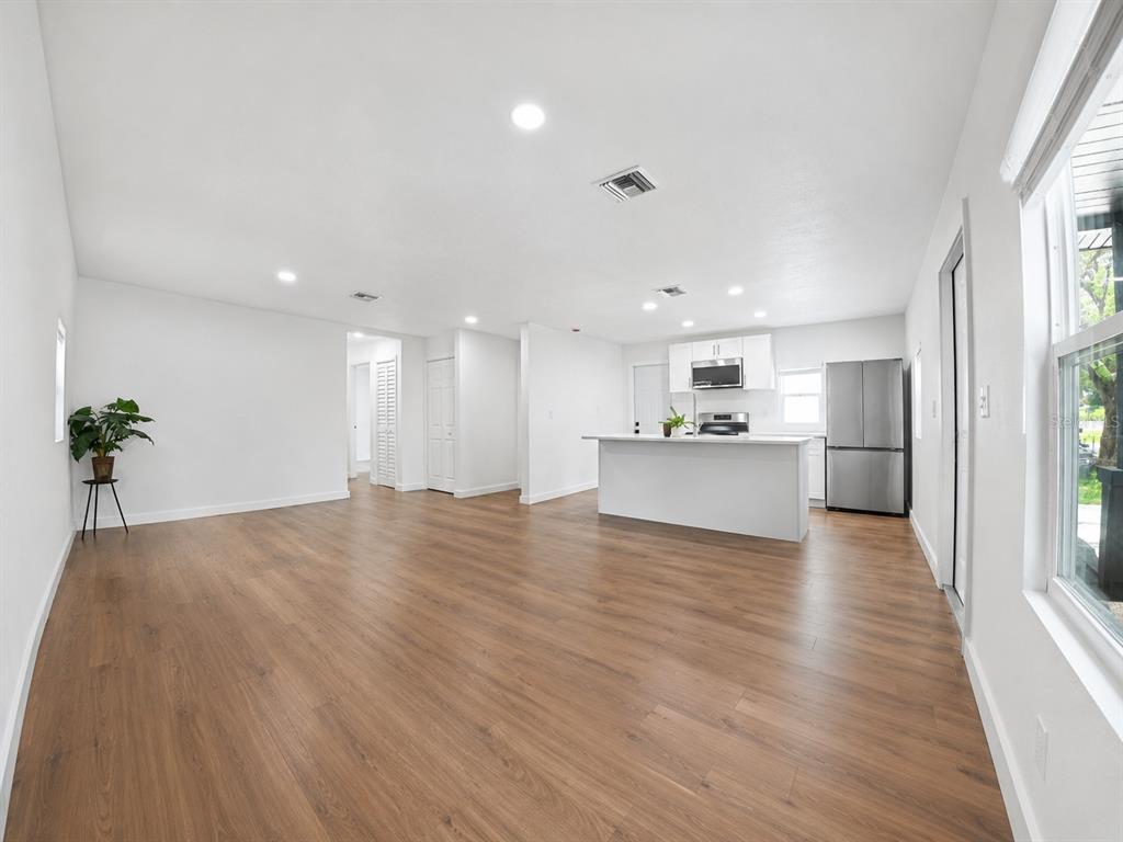 An open-concept living area features wood-look flooring, white walls, and a kitchen with white cabinets — 9212 N BROOKS STREET, TAMPA, FL