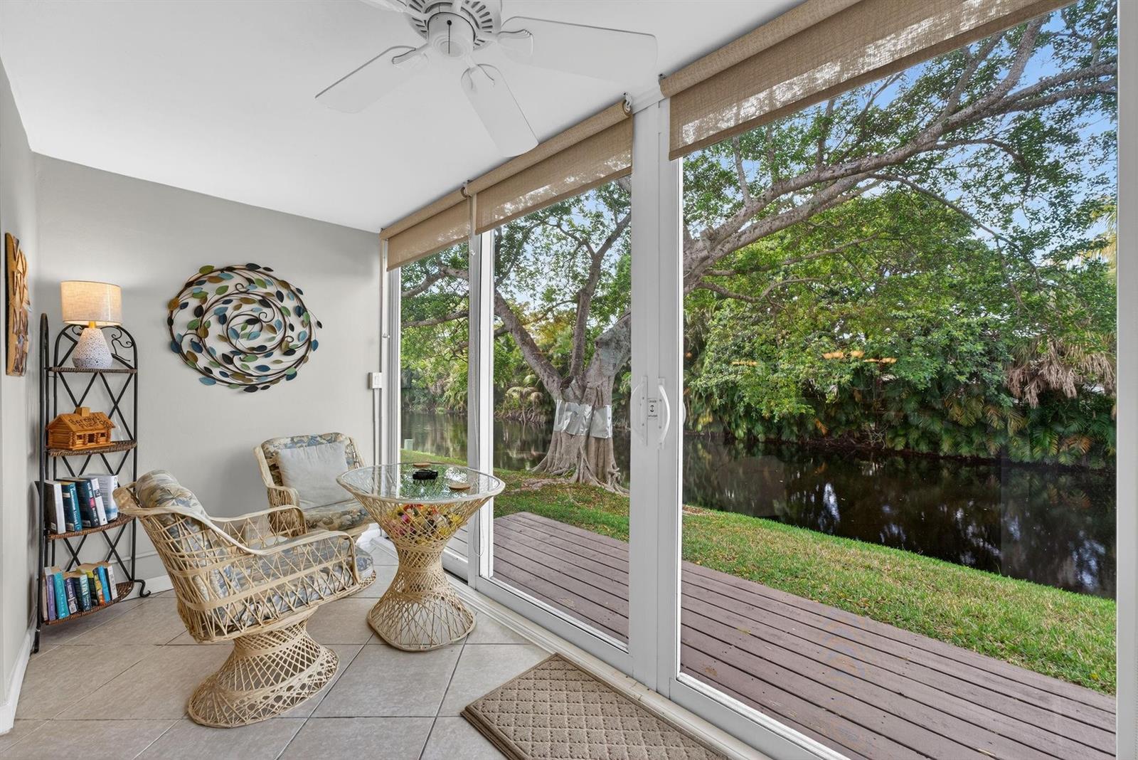 A sunroom with wicker furniture and sliding glass doors overlooking a canal and trees — 101 NW 76th Avenue # 102, Margate FL 33063, MARGATE, FL
