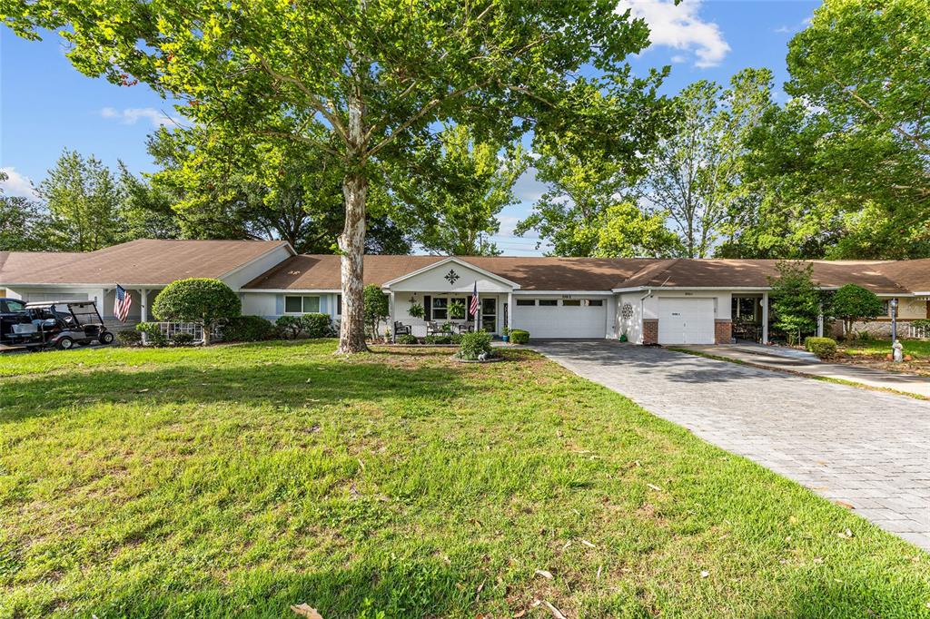 A single-story house with a paved driveway, two garage doors, and large shade trees — 8900 SW 97TH LANE ROAD UNIT H, OCALA, FL