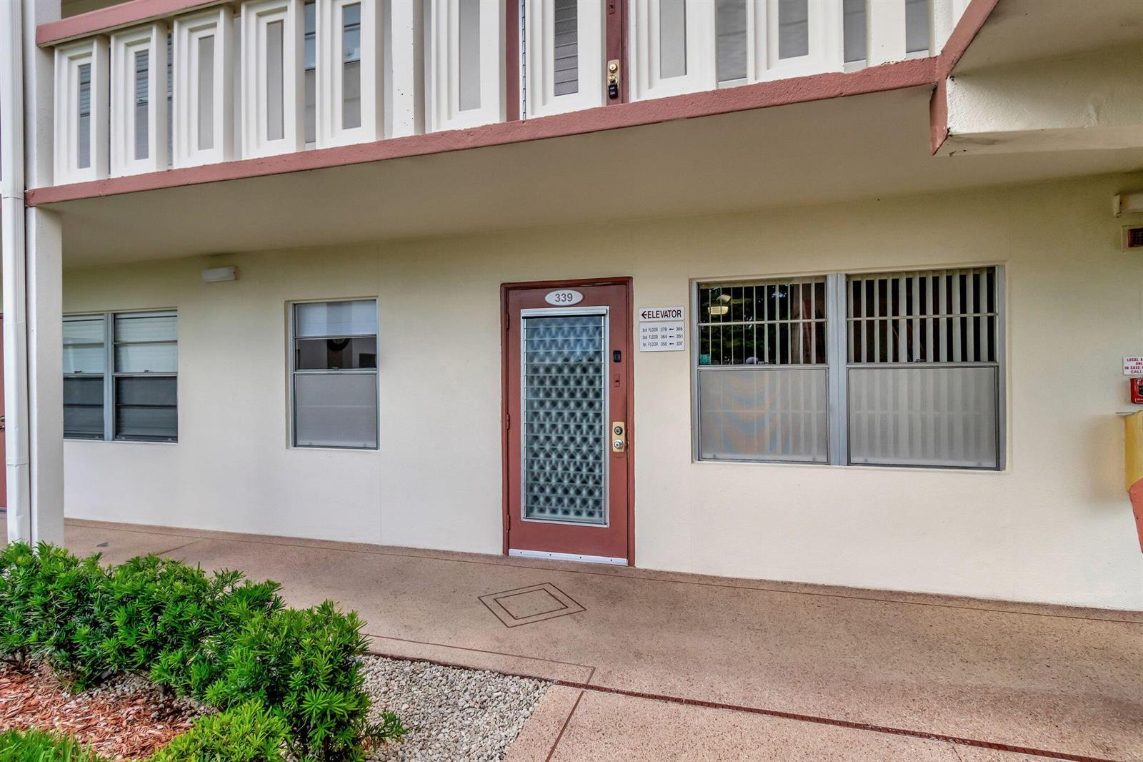 A ground-level exterior view of a building entrance with a red-framed door and elevator signage — 339 Preston I, Boca Raton FL 33434, BOCA RATON, FL