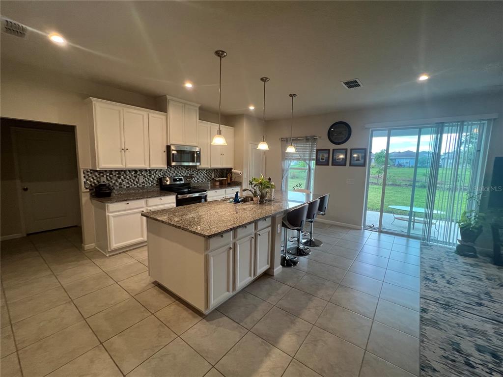 A kitchen features white cabinetry, granite countertops, a central island, and tile flooring — 2937 SLOUGH CREEK DRIVE, KISSIMMEE, FL