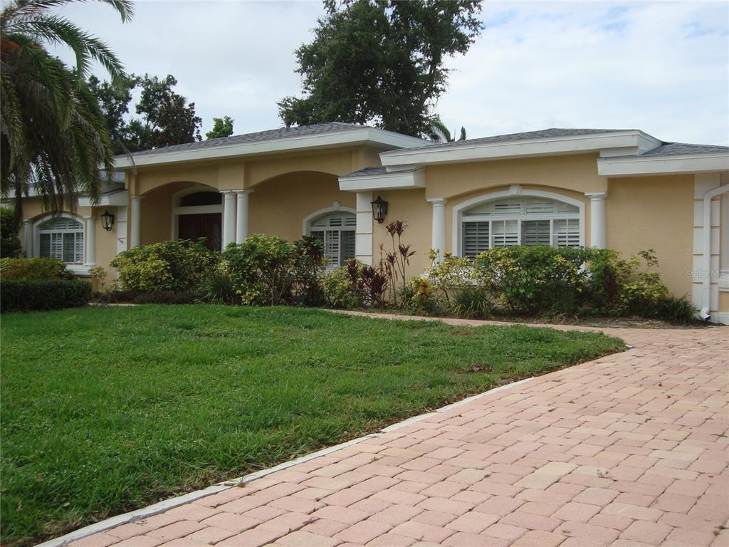 A single-story house with a light yellow exterior, arched windows, and a paved driveway — 601 PALM AVENUE, BELLEAIR, FL