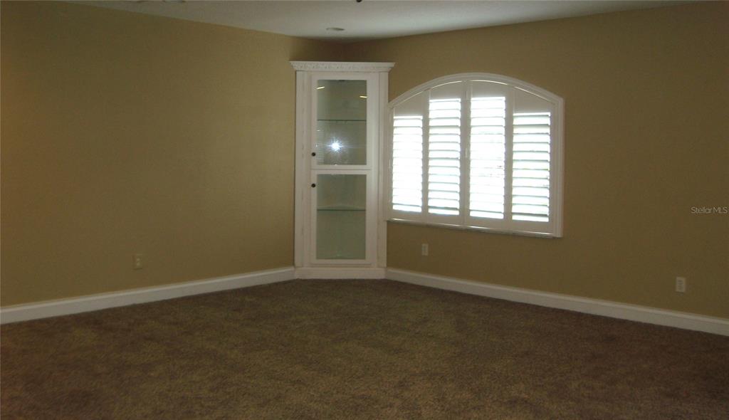 An empty room features beige walls, brown carpeting, a corner display cabinet, and arched shutters — 601 PALM AVENUE, BELLEAIR, FL