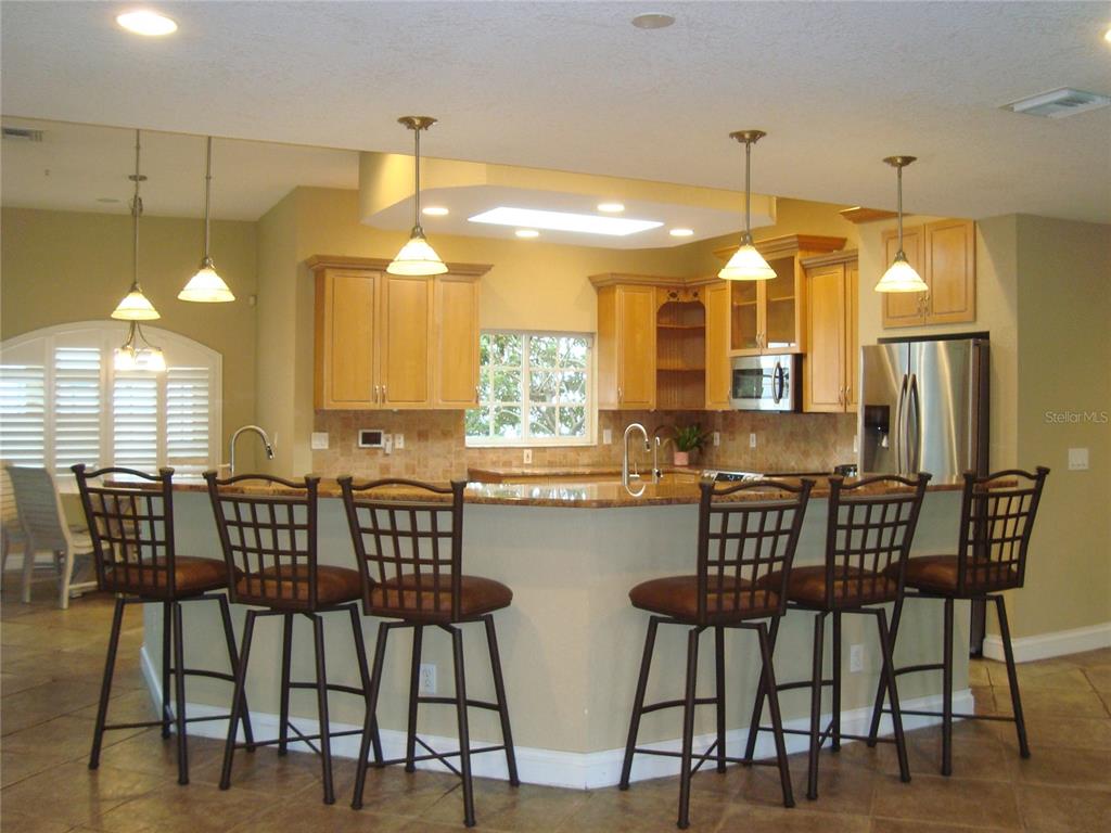 A kitchen features light wood cabinets, granite countertops, a breakfast bar, and six bar stools — 601 PALM AVENUE, BELLEAIR, FL