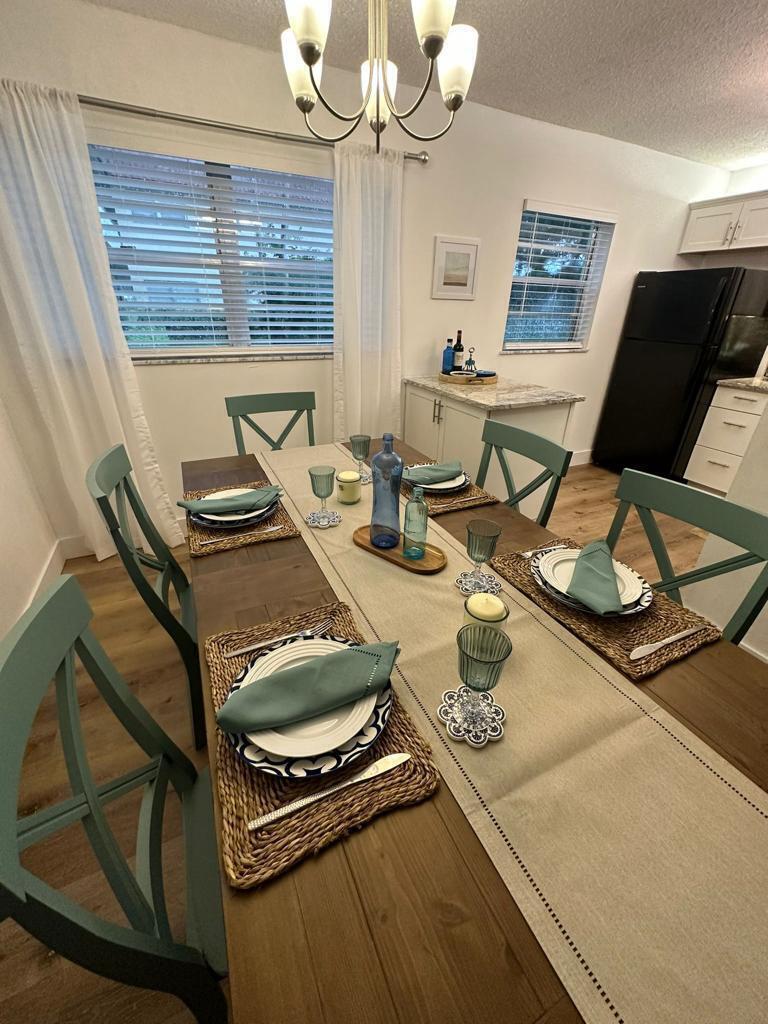A dining room features a wooden table with place settings, teal chairs, and a chandelier — 86 Crooked Tree Lane # 102, Vero Beach FL 32962, VERO BEACH, FL