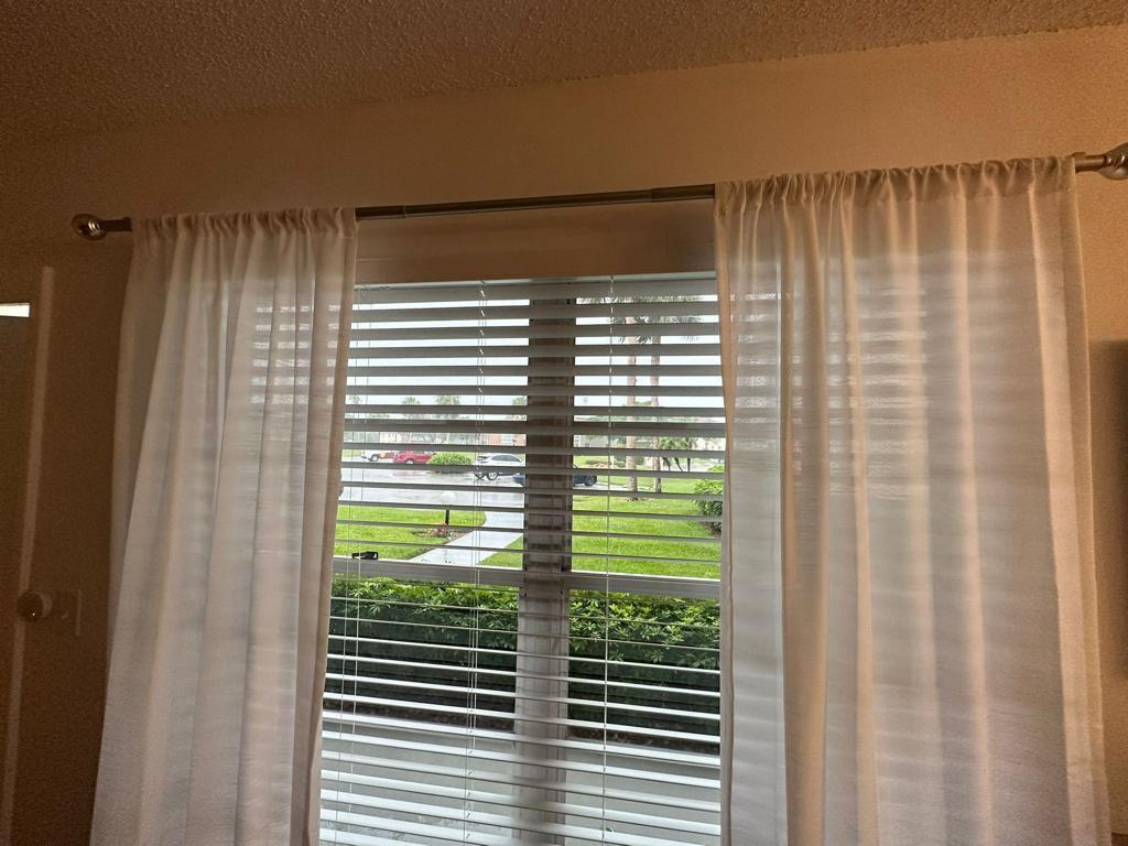 A window with white horizontal blinds and sheer white curtains hanging on a metal rod — 86 Crooked Tree Lane # 102, Vero Beach FL 32962, VERO BEACH, FL