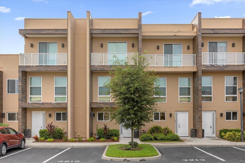 A row of modern three-story townhouses with tan stucco facades and private balconies — 3215 BRASILIA AVENUE, KISSIMMEE, FL