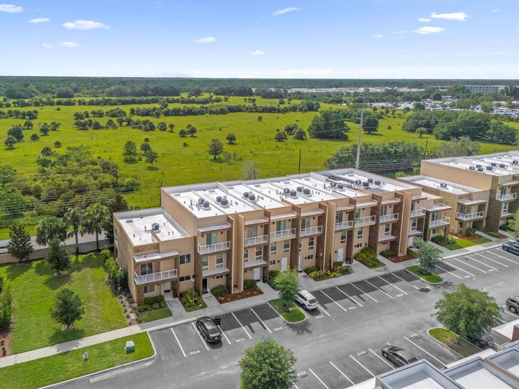 An aerial view shows a multi-story apartment building with a parking lot and grassy field — 3215 BRASILIA AVENUE, KISSIMMEE, FL
