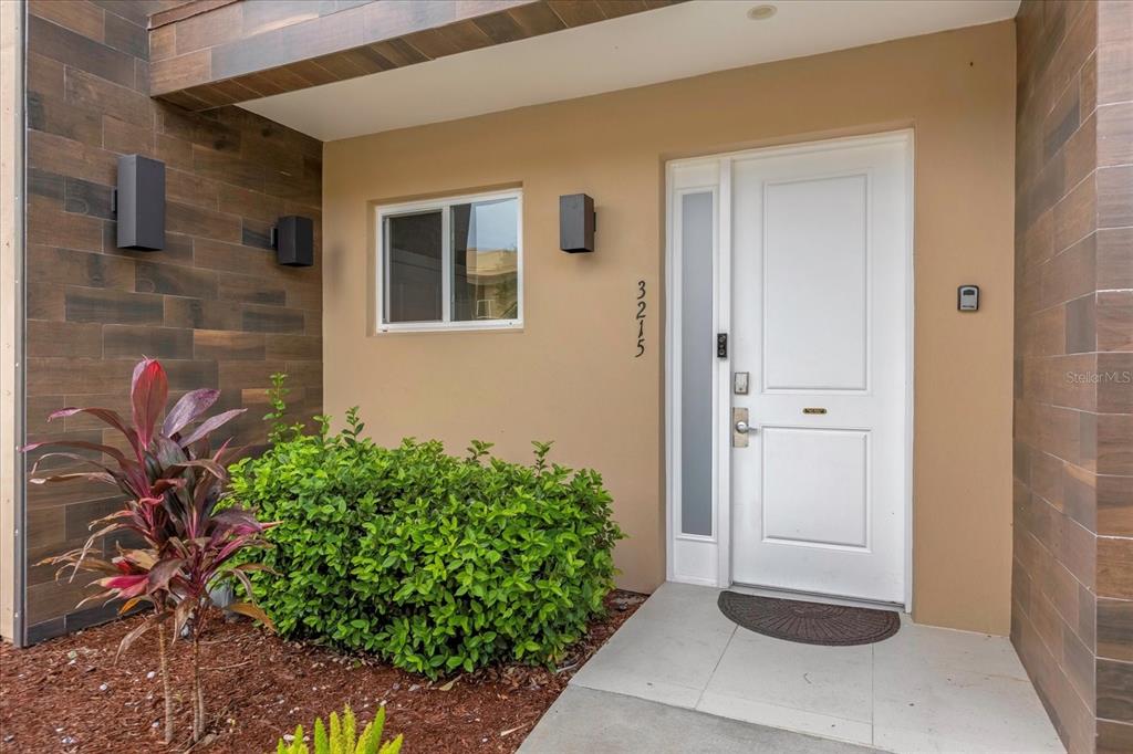 A white front door with a side light is set against a tan wall — 3215 BRASILIA AVENUE, KISSIMMEE, FL