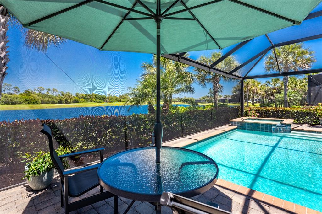 A patio with a pool, hot tub, and umbrella overlooks a lake and golf course — 25180 LONGMEADOW DRIVE, PUNTA GORDA, FL
