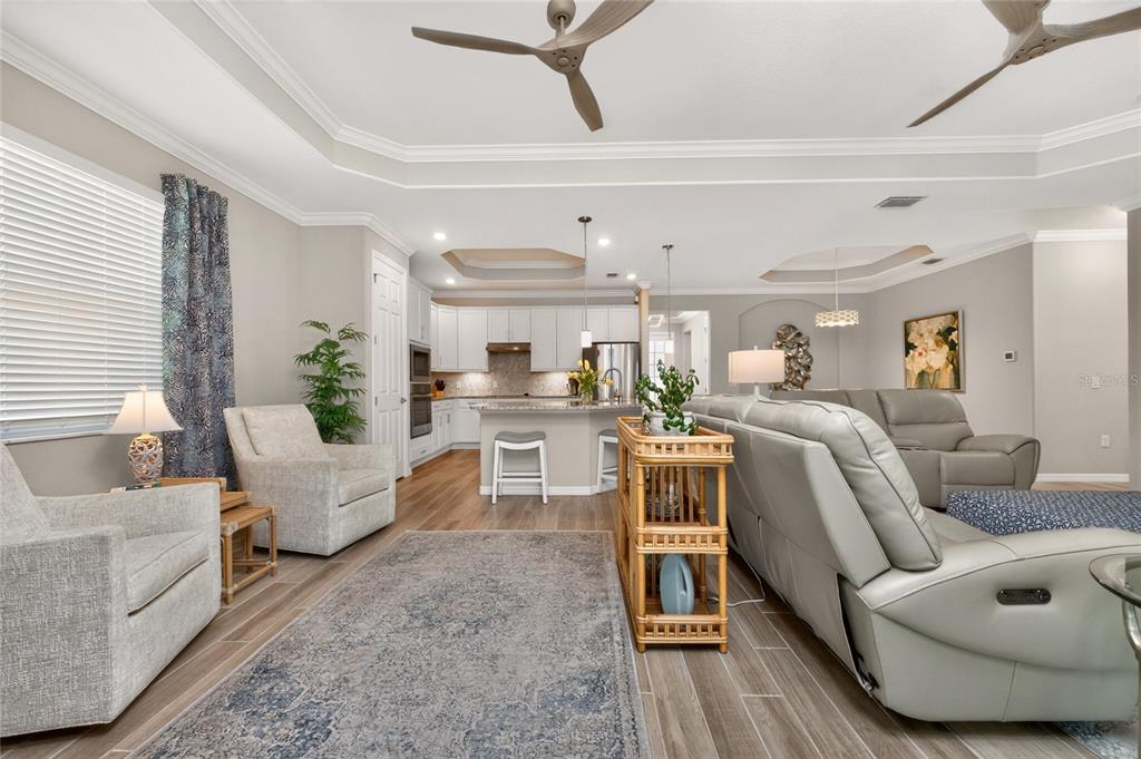 An open-concept living room and kitchen featuring light gray walls, tile flooring, and ceiling fans — 25180 LONGMEADOW DRIVE, PUNTA GORDA, FL