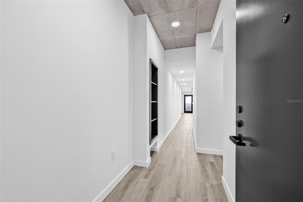 A long, narrow hallway features light wood flooring, white walls, and an exposed concrete ceiling — 221 MAIN STREET N UNIT B2-1010, ST PETERSBURG, FL