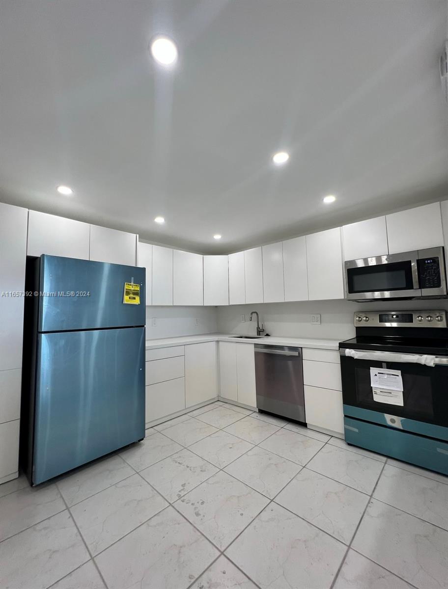 A kitchen features white flat-panel cabinets, stainless steel appliances, and light-colored tiled flooring — 13499 Biscayne Blvd # 1405, North Miami FL 33181, NORTH MIAMI, FL