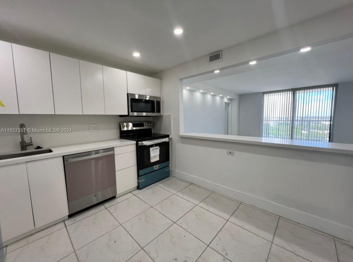 A modern kitchen features white cabinets, stainless steel appliances, and a pass-through window to living — 13499 Biscayne Blvd # 1405, North Miami FL 33181, NORTH MIAMI, FL