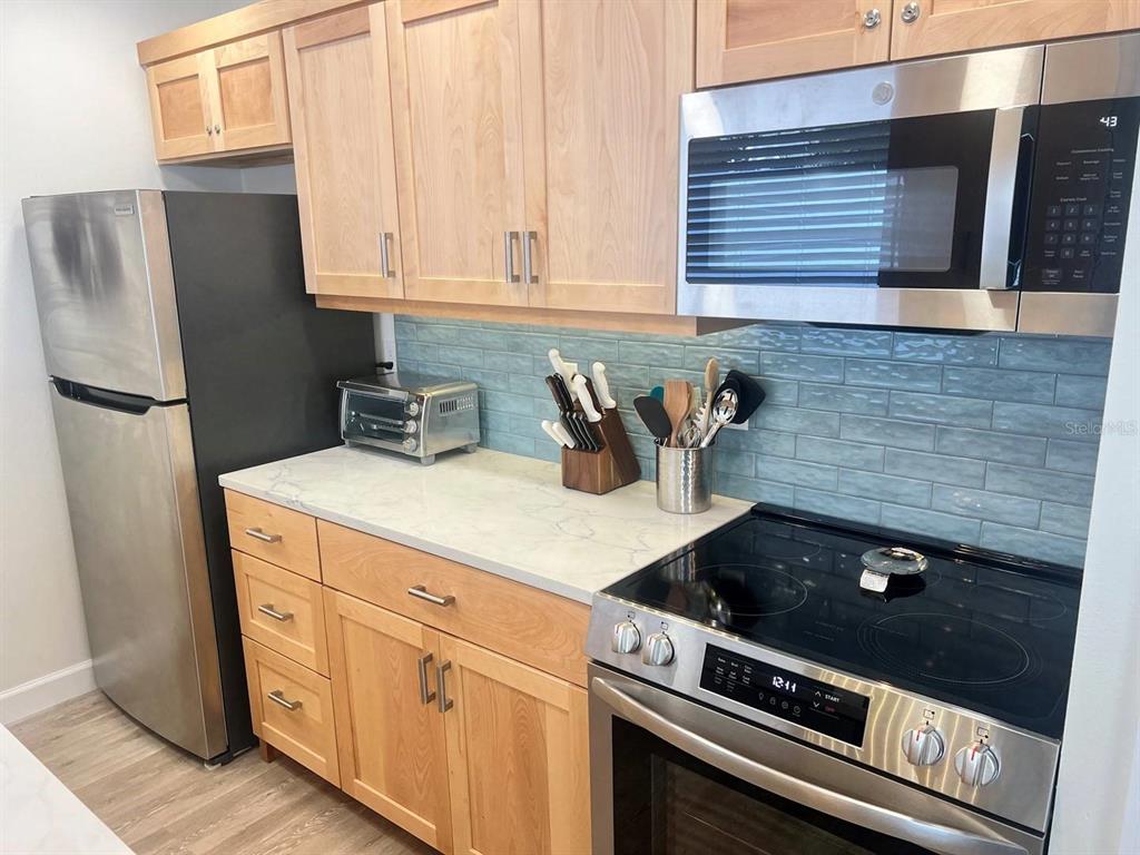 A kitchen features light wood cabinets, stainless steel appliances, a white countertop, and blue backsplash — 6020 MIDNIGHT PASS ROAD UNIT 36, SARASOTA, FL