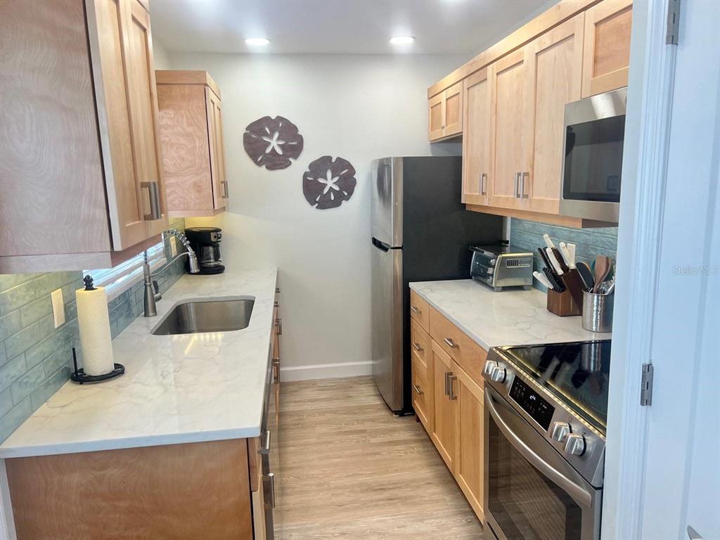 A galley kitchen features light wood cabinets, white countertops, and stainless steel appliances — 6020 MIDNIGHT PASS ROAD UNIT 36, SARASOTA, FL