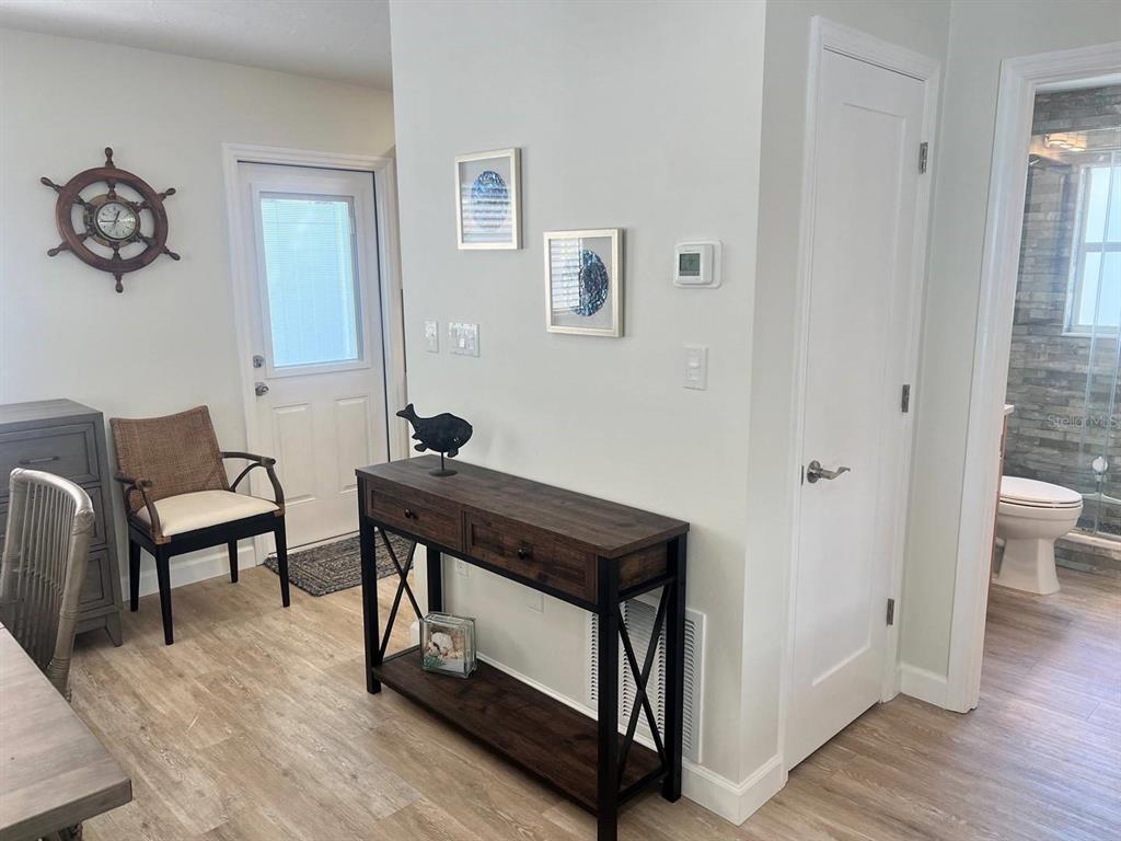A hallway features wood-look flooring, a console table, a chair, and a door to a bathroom — 6020 MIDNIGHT PASS ROAD UNIT 36, SARASOTA, FL