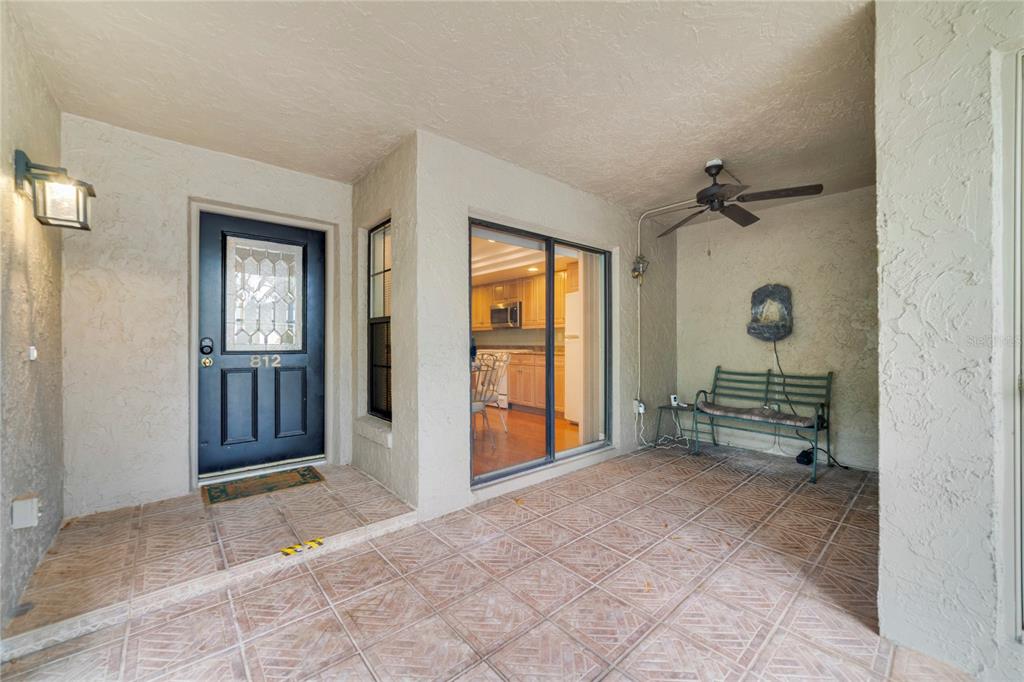 A covered patio features tiled flooring, a dark front door, a sliding glass door, and a bench — 1055 KENSINGTON PARK DRIVE UNIT 812, ALTAMONTE SPRINGS, FL