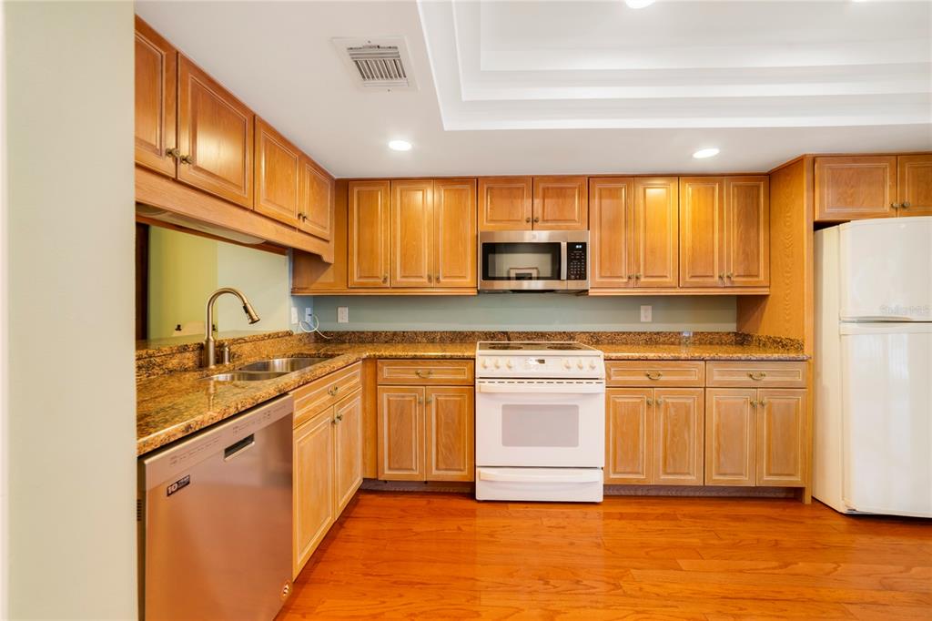 A kitchen features wood cabinets, granite countertops, a white stove, and a stainless steel dishwasher — 1055 KENSINGTON PARK DRIVE UNIT 812, ALTAMONTE SPRINGS, FL
