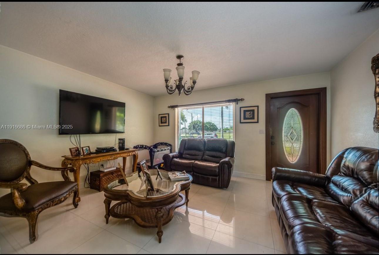 A living room features tile flooring, a dark leather sofa, a coffee table, and a chandelier — 10260 SW 48th St, Miami FL 33165, MIAMI, FL