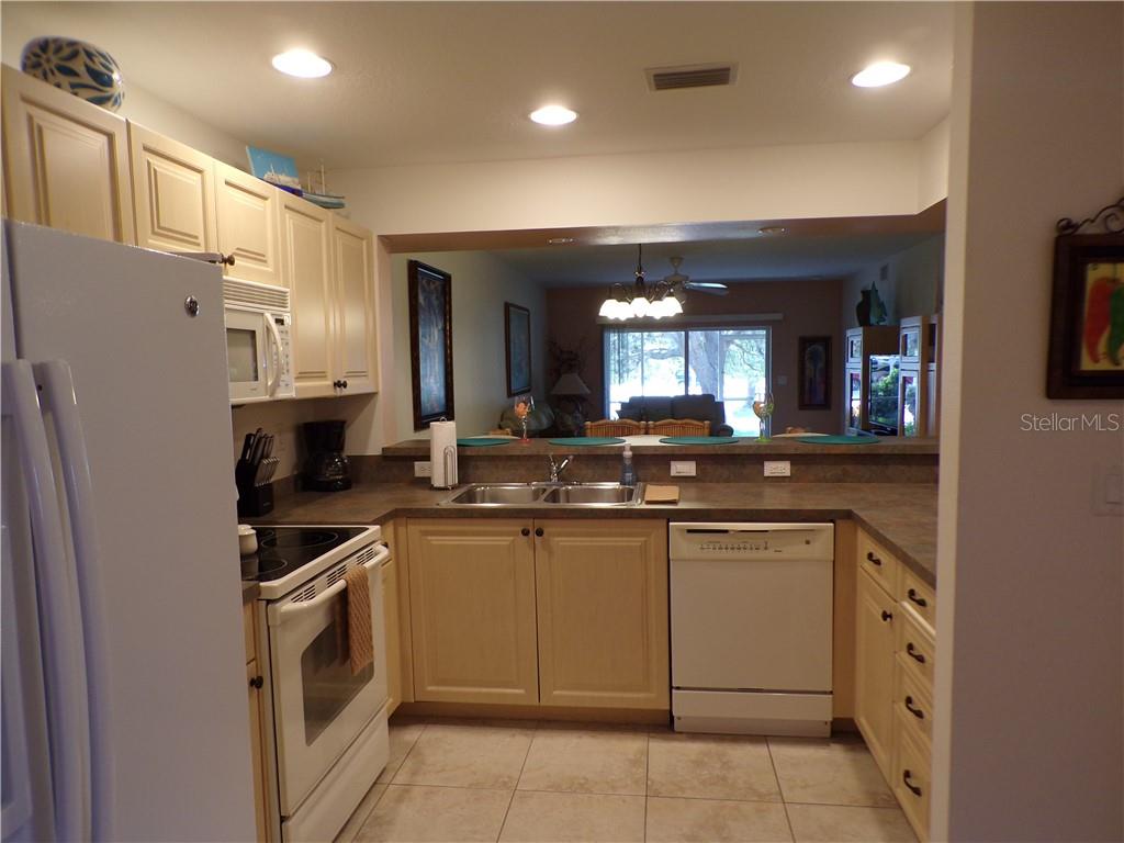 A kitchen with light-colored cabinets, white appliances, and a pass-through window to the living area — 1462 RIO DE JANEIRO AVENUE UNIT B103, PUNTA GORDA, FL