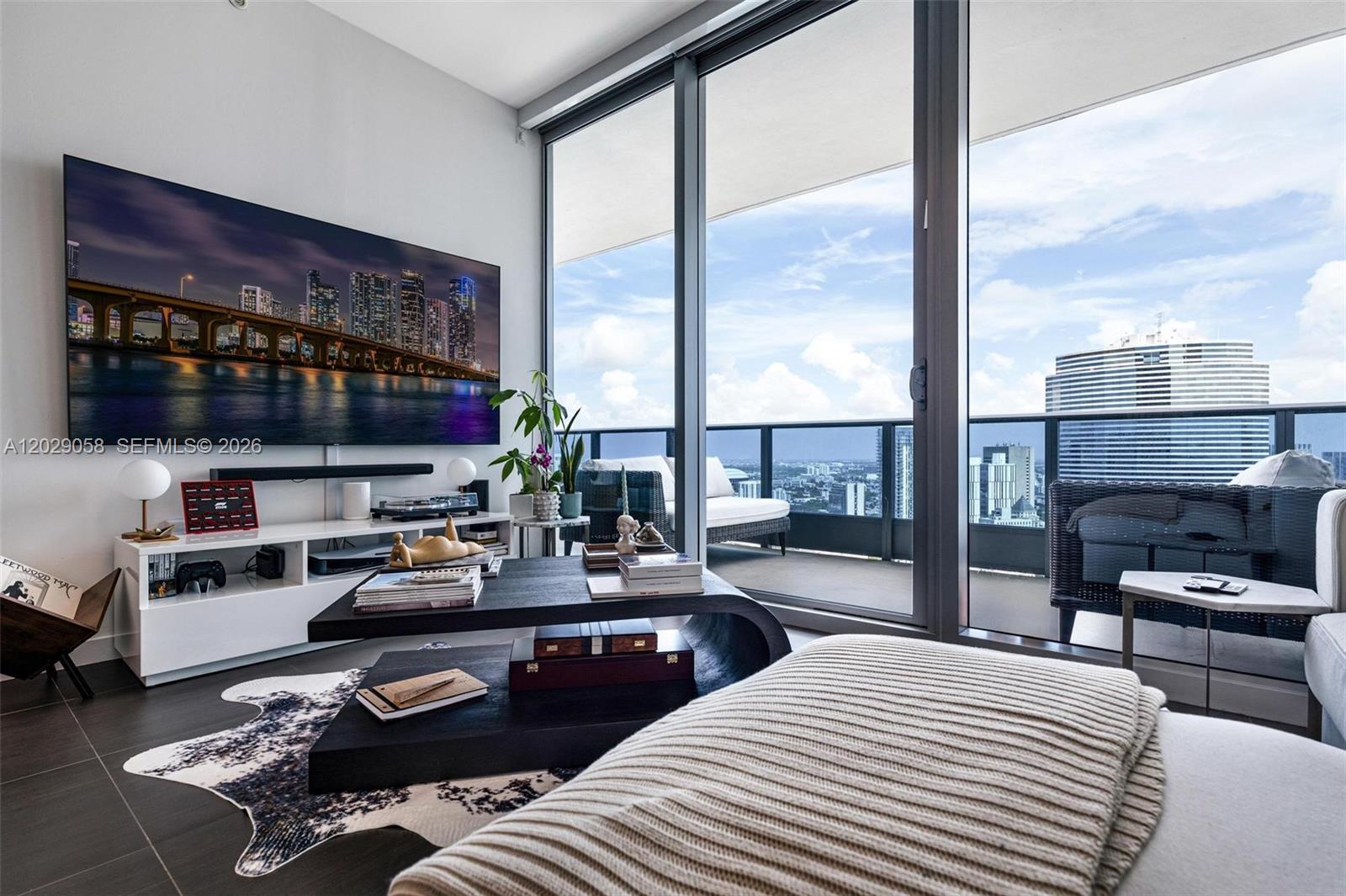 A modern living room features a large television, a black coffee table, and a balcony view — 200 Biscayne Boulevard Way # 4812, Miami FL 33131, MIAMI, FL