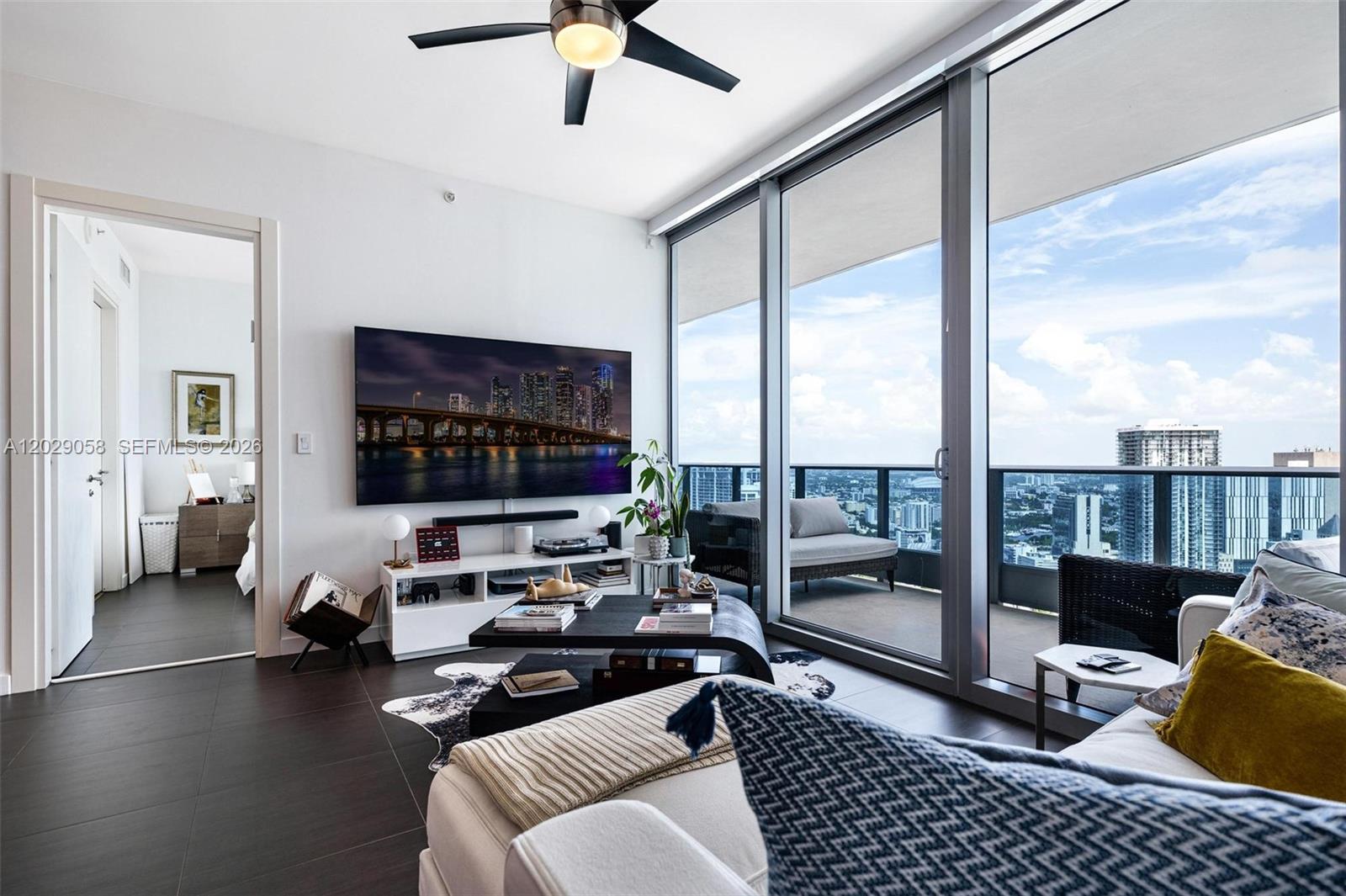 A modern living room features dark tile floors, a large television, and floor-to-ceiling balcony windows — 200 Biscayne Boulevard Way # 4812, Miami FL 33131, MIAMI, FL