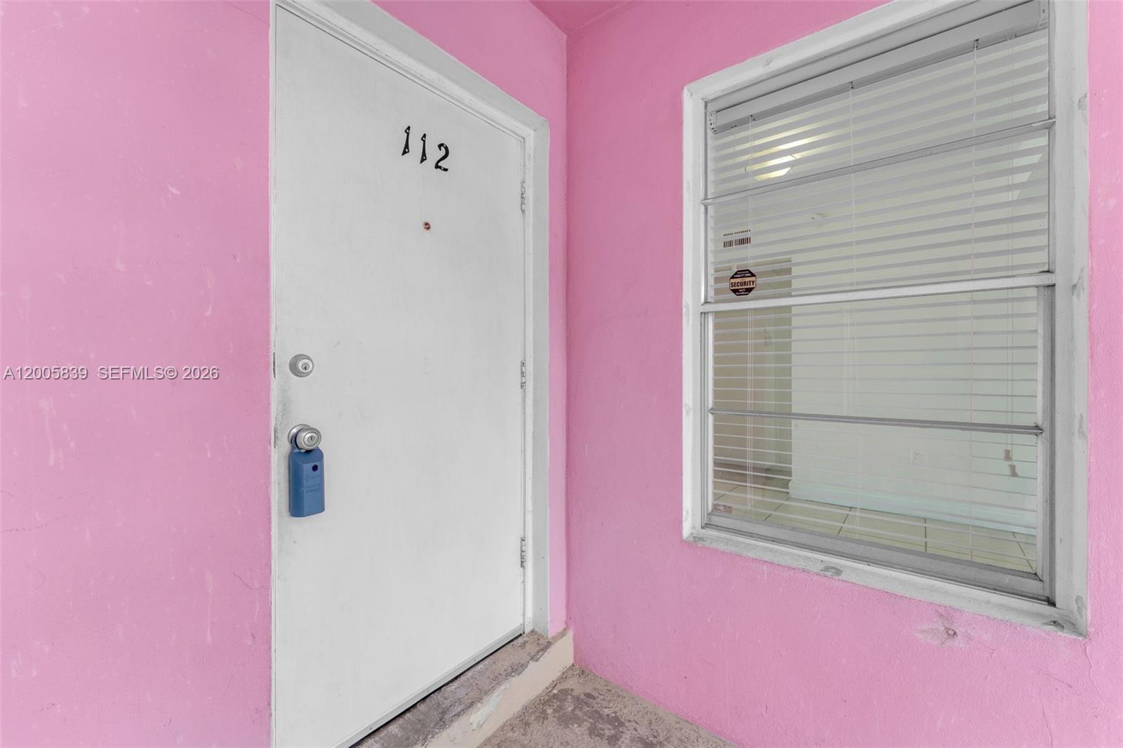 A white door labeled 112 and a window with blinds are set in a pink wall — 7560 SW 82nd St # G112, Miami FL 33143, MIAMI, FL