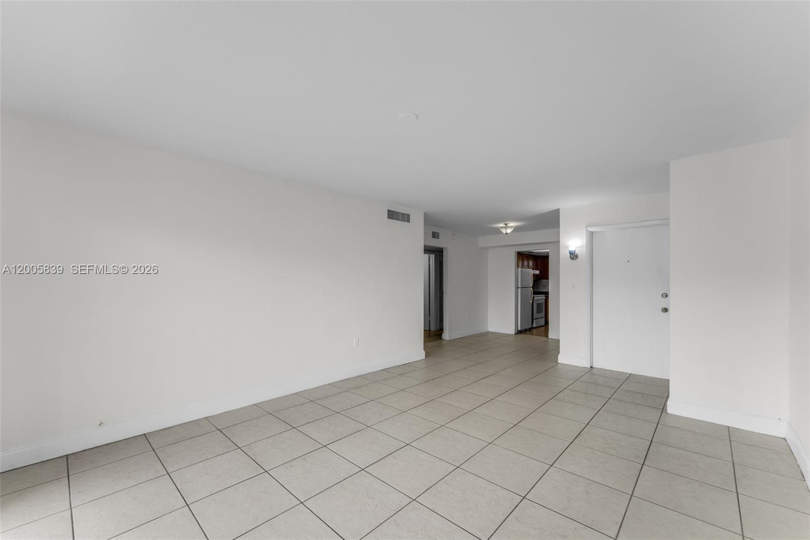 An empty room with light-colored tile flooring, white walls, and a view into a kitchen — 7560 SW 82nd St # G112, Miami FL 33143, MIAMI, FL