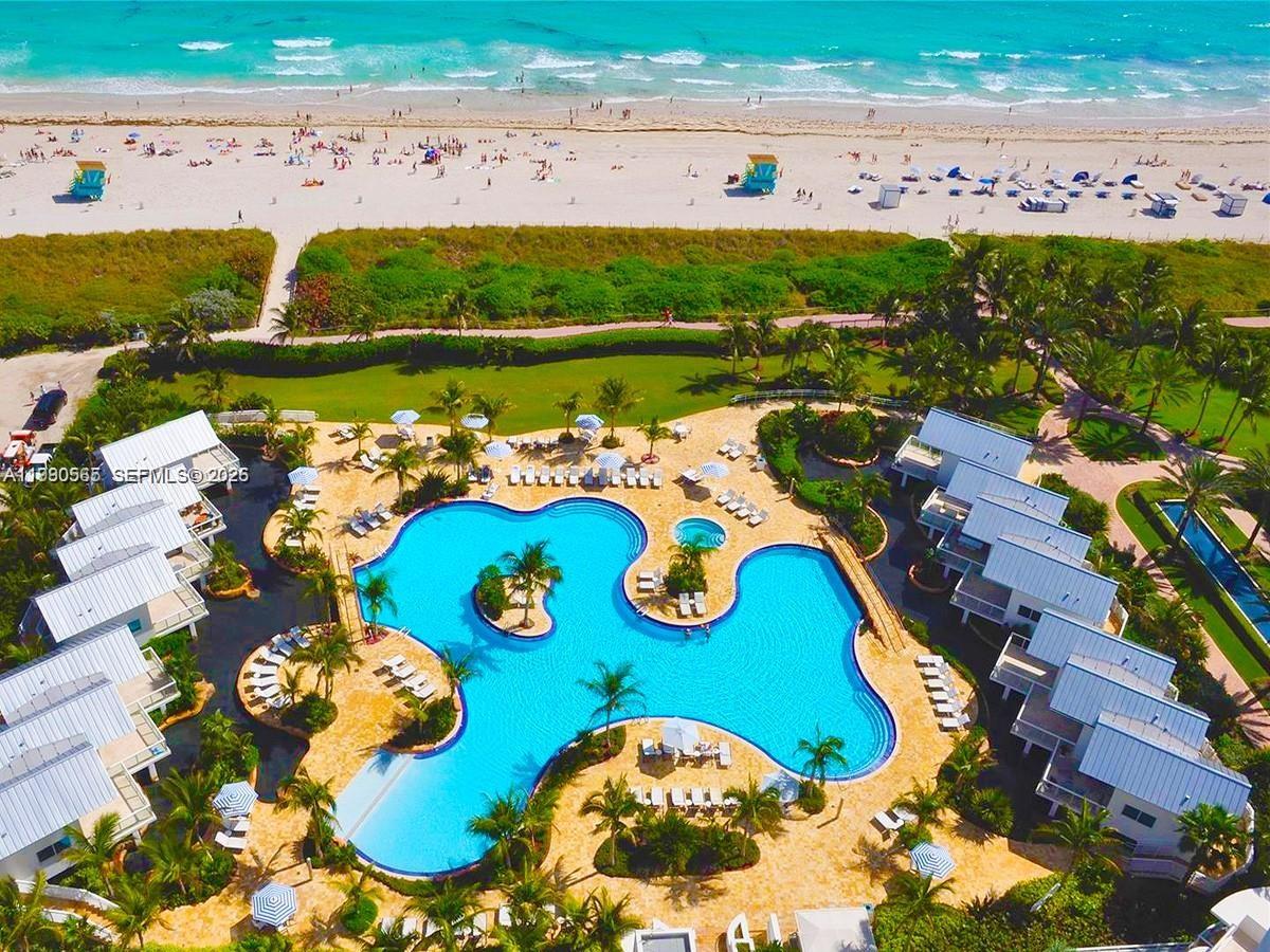 An aerial view shows a resort swimming pool surrounded by buildings, palm trees, and beach — 50 S Pointe Dr # 504, Miami Beach FL 33139, MIAMI BEACH, FL